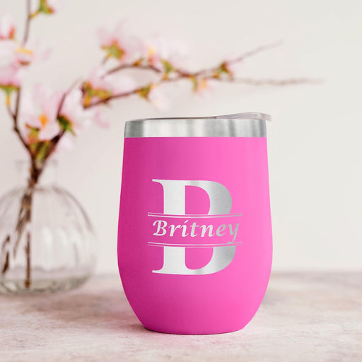 Pink wine tumbler with silver lid and 'Britney' engraving on a light wooden surface with floral background