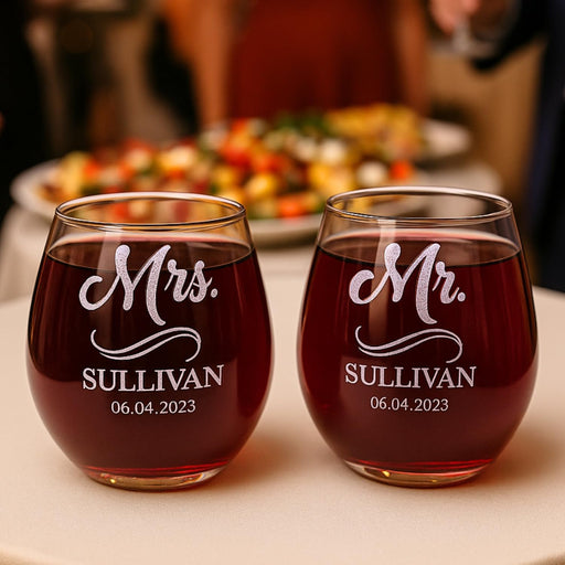 Two wine glasses with 'Mr.' and 'Mrs.' etched on them, filled with red wine, on a table with a blurred background.