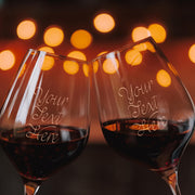 Two wine glasses with personalized text against a blurred lights background
