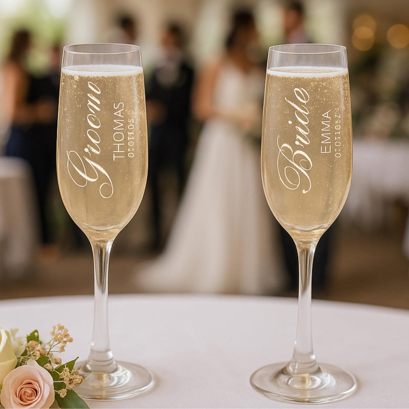 Two champagne flutes with 'Groom' and 'Bride' engraved names on a blurred wedding background.