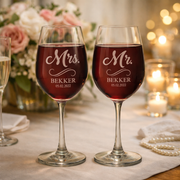 Two wine glasses with 'Mr.' and 'Mrs.' inscriptions on a table with candles and flowers.