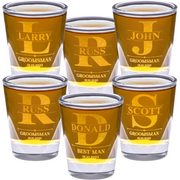 Set of personalized shot glasses with names and roles engraved, filled with a yellow liquid.