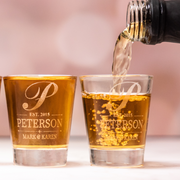 Personalized whiskey shot glasses engraved with initial, family name, and established date, filled with golden whiskey.