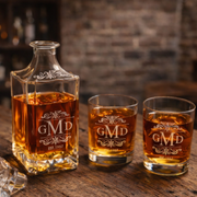 Two glasses and a decanter of whiskey with 'GMD' branding on a wooden surface.